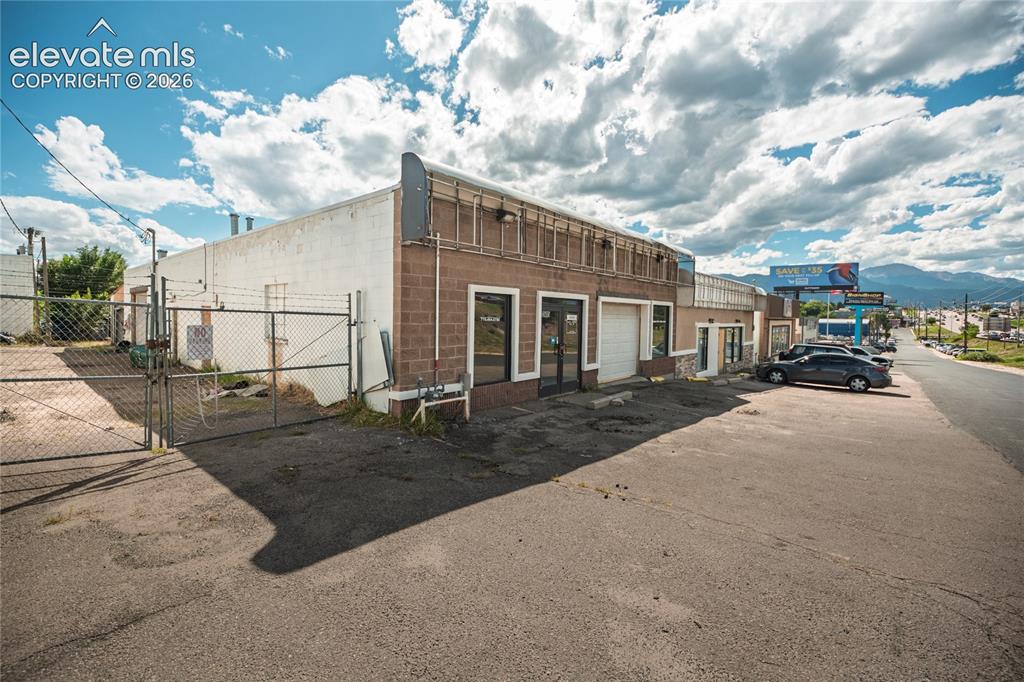 Image 3 of 50: Brick exterior with a roll-up garage door, multiple entryways, and a paved