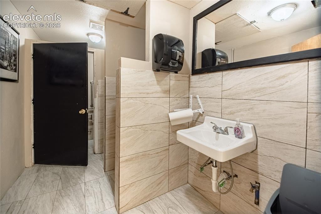 Image 31 of 50: White wall-mounted sink with chrome fixtures, set against light-toned tiled