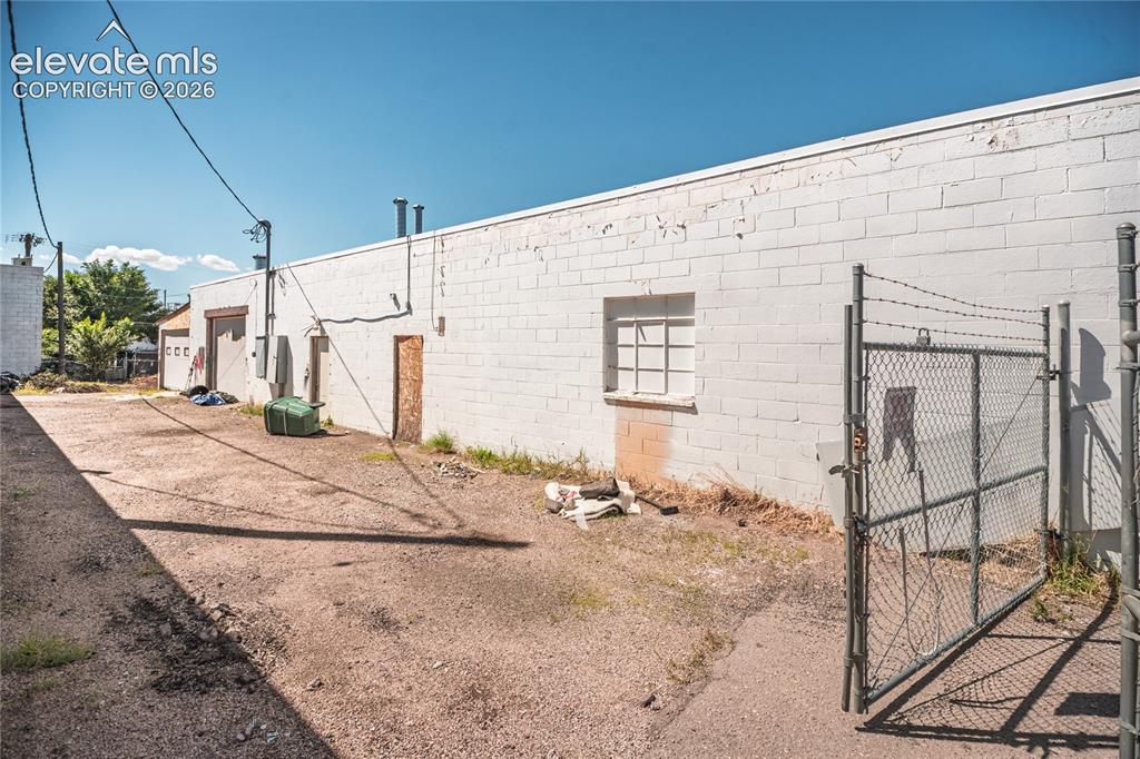 Image 5 of 50: White brick exterior with a chain-link fence and barbed wire