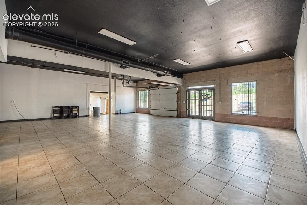 Image 8 of 50: Spacious interior with neutral-toned tile flooring, exposed ductwork, brick