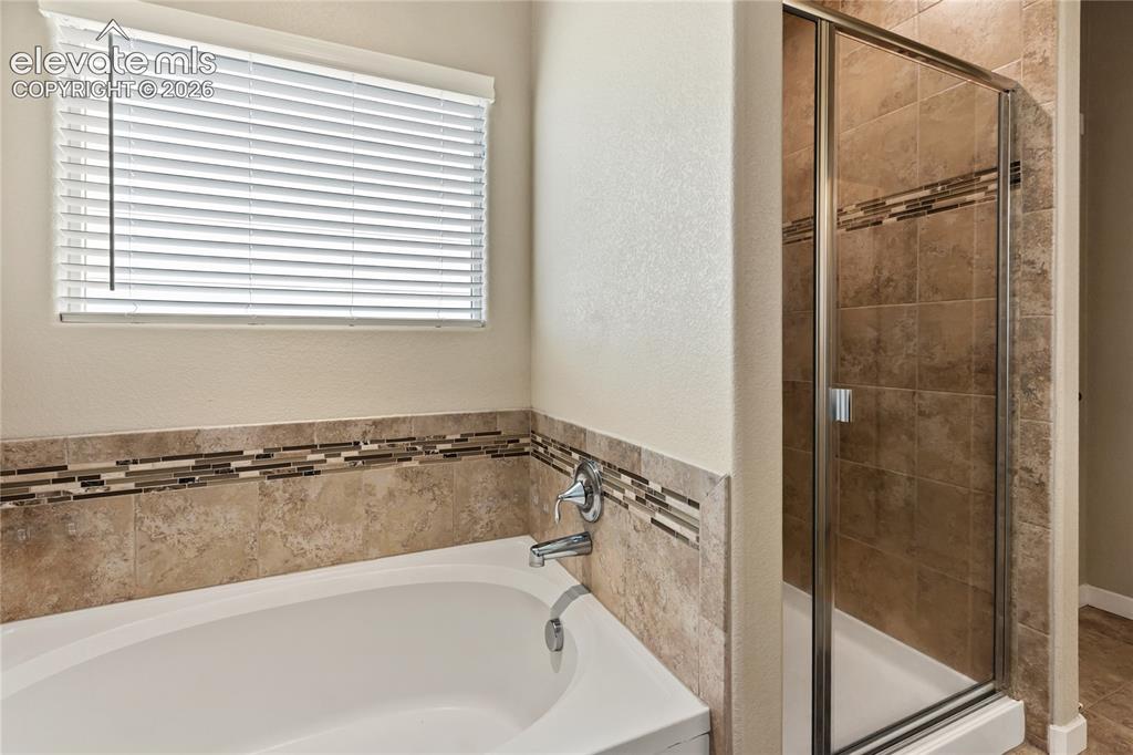Image 10 of 32: Soaking tub and standing shower with a tiled surround featuring a decorativ