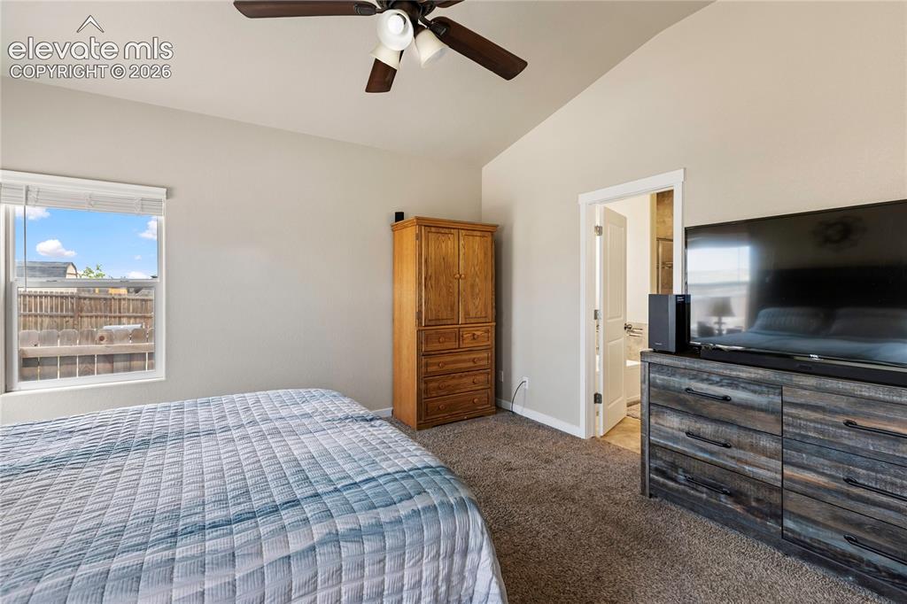 Image 13 of 30: Vaulted ceiling with a ceiling fan, carpeted flooring, and a window with bl