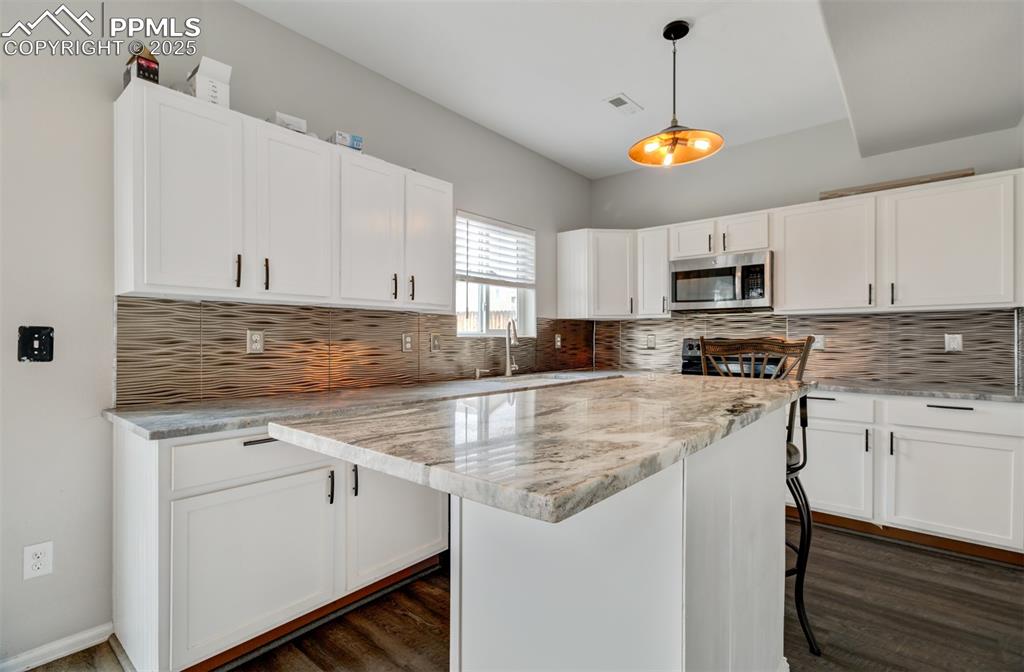 Image 2 of 35: Kitchen featuring white cabinets, stainless steel microwave, a kitchen isla
