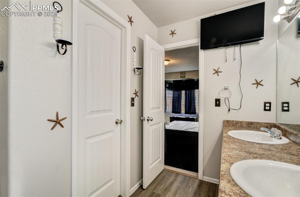 Image 23 of 35: Ensuite bathroom with double vanity, a sink, connected bathroom, and wood f