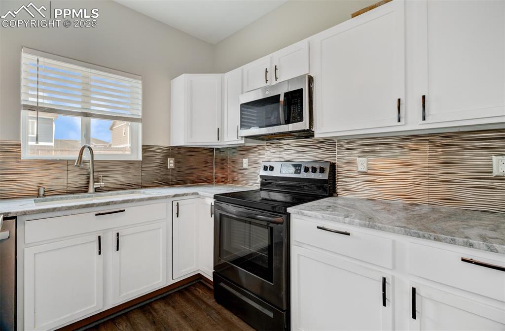 Image 6 of 35: Kitchen with black electric range oven, white cabinetry, stainless steel mi