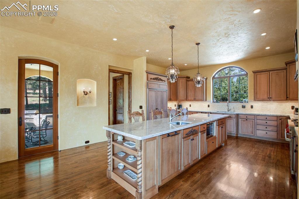 Image 17 of 50: Kitchen with stunning light fixtures, dark hardwood floors, tasteful backsp