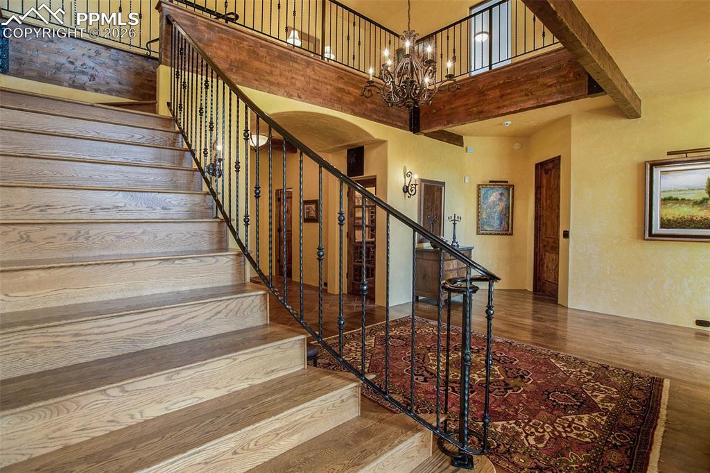 Image 7 of 50: Staircase featuring hardwood floors, a towering ceiling, and a stunning cha