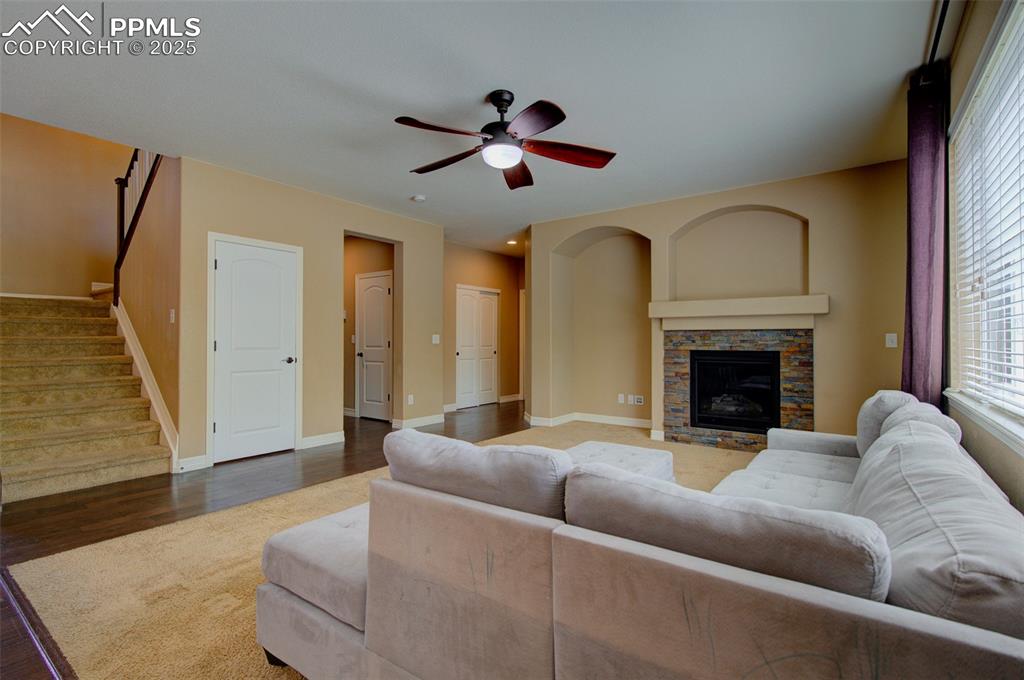 Image 12 of 50: Great room with stone gas fireplace and a ceiling fan