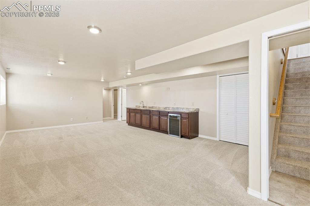 Image 32 of 43: Finished basement featuring bar with sink, light colored carpet, and wine c