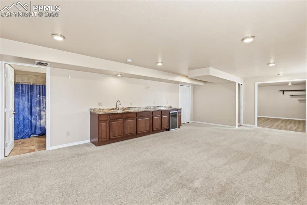 Image 33 of 43: Indoor wet bar featuring light colored carpet and wine cooler