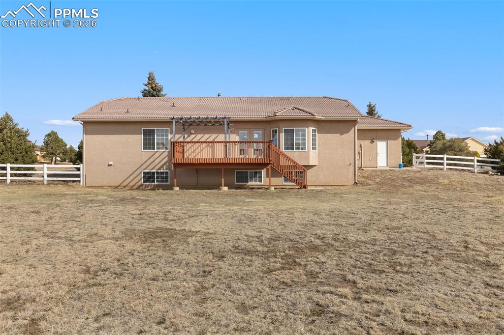 Image 43 of 43: Back of house featuring a fenced backyard, a deck, a tile roof, and stucco 