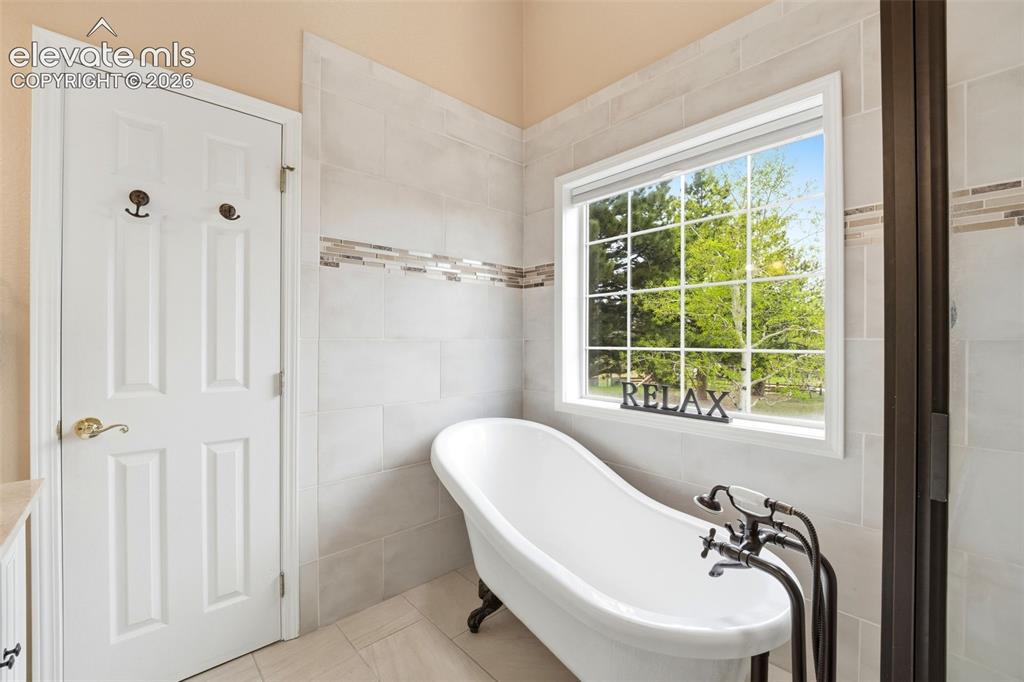 Image 24 of 41: Freestanding clawfoot tub with floor-mounted fixtures, set against a tiled