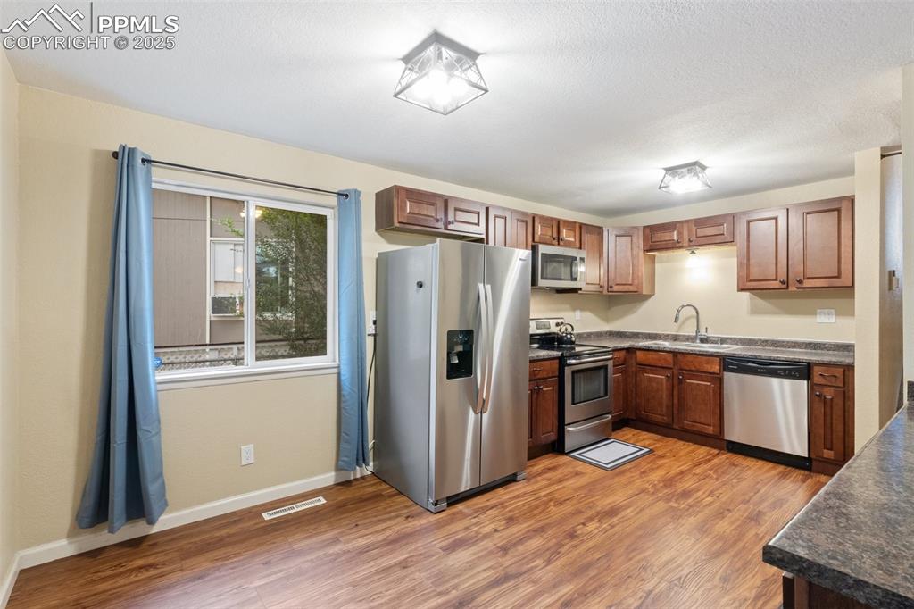 Image 14 of 35: Kitchen with stainless steel appliances, dark countertops, light wood finis