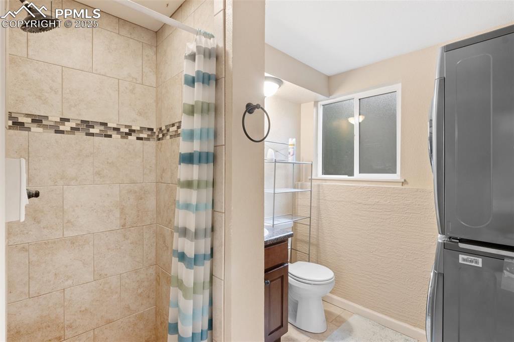 Image 20 of 35: Full bath featuring stacked washer / dryer, tiled shower, tile patterned fl
