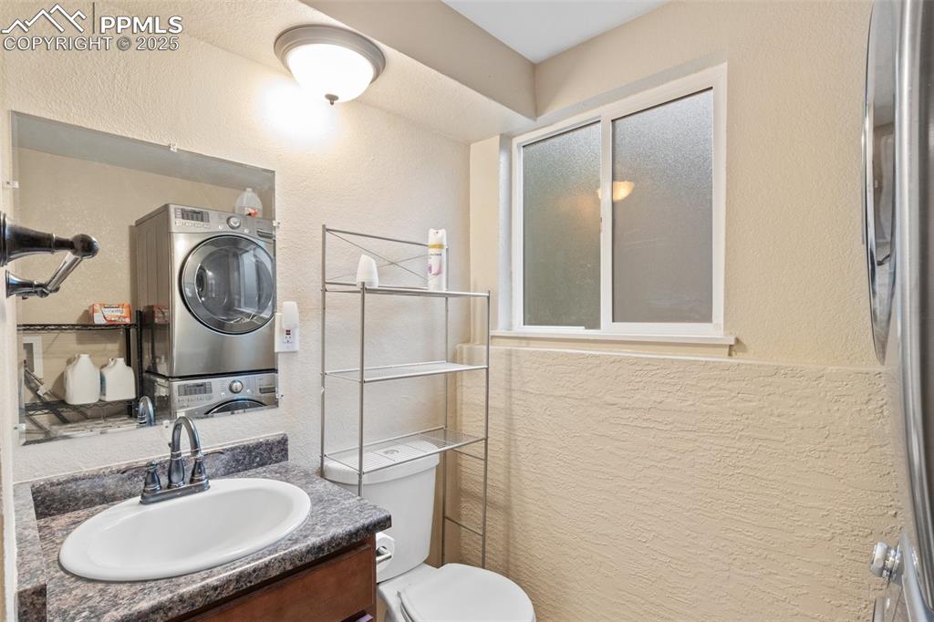 Image 21 of 35: Full bath featuring stacked washing machine and dryer, vanity, a textured w