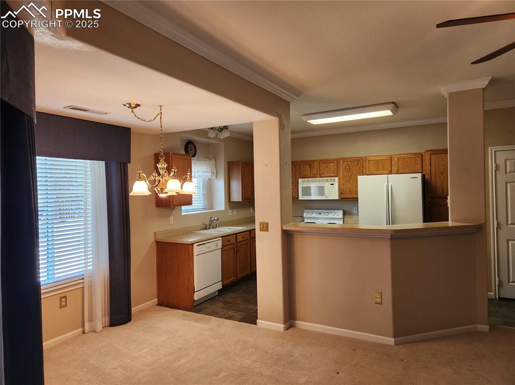 Image 14 of 19: Kitchen with white appliances, brown cabinets, a chandelier, dark colored c