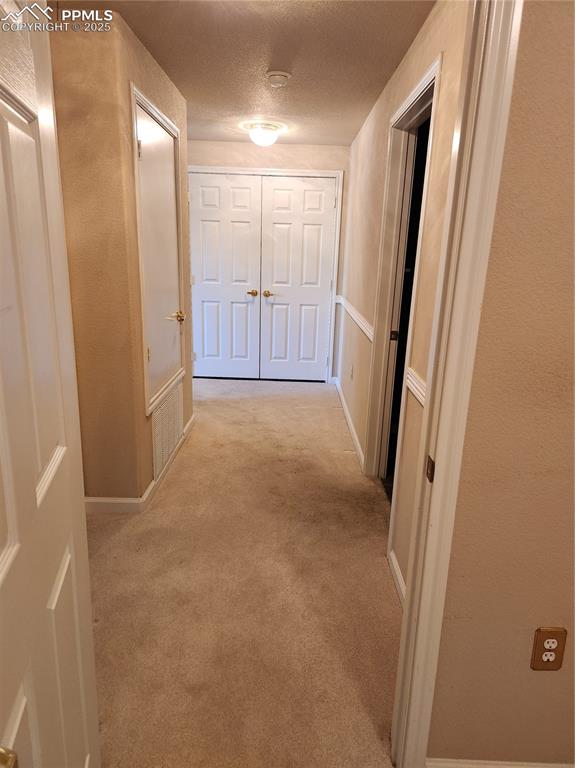 Image 17 of 19: Hall featuring light carpet, a textured ceiling, and a textured wall