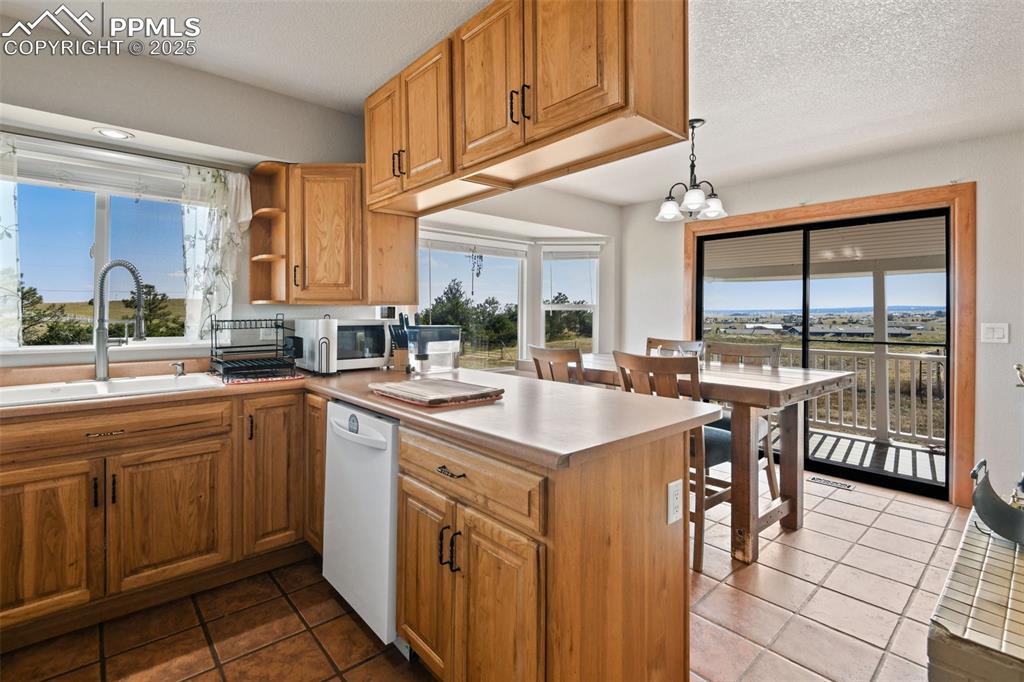 Image 10 of 40: Kitchen featuring decorative light fixtures, brown cabinets, dark tile patt