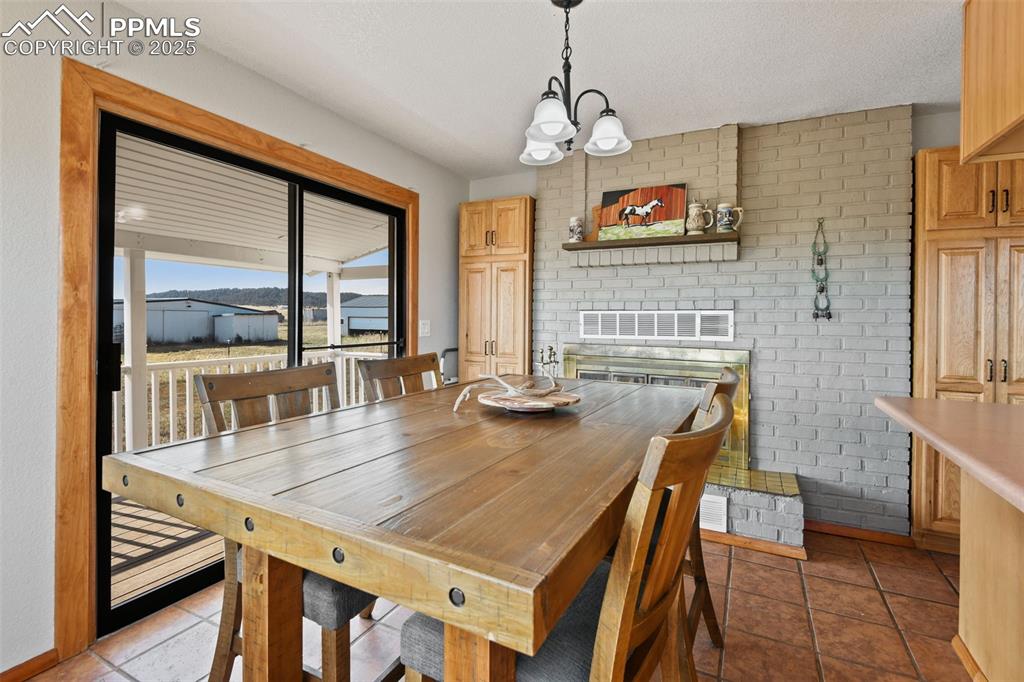 Image 13 of 40: Tiled dining space featuring a chandelier, a fireplace, and brick wall