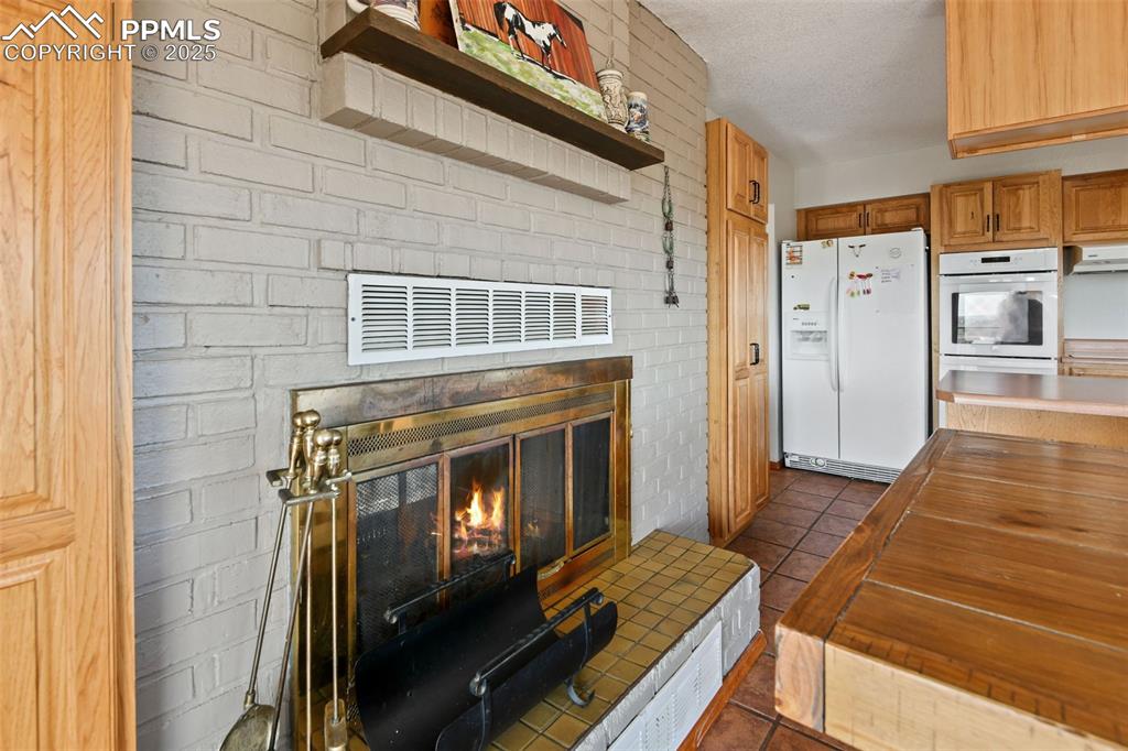 Image 14 of 40: Kitchen with white appliances, dark tile patterned floors, wood counters, u