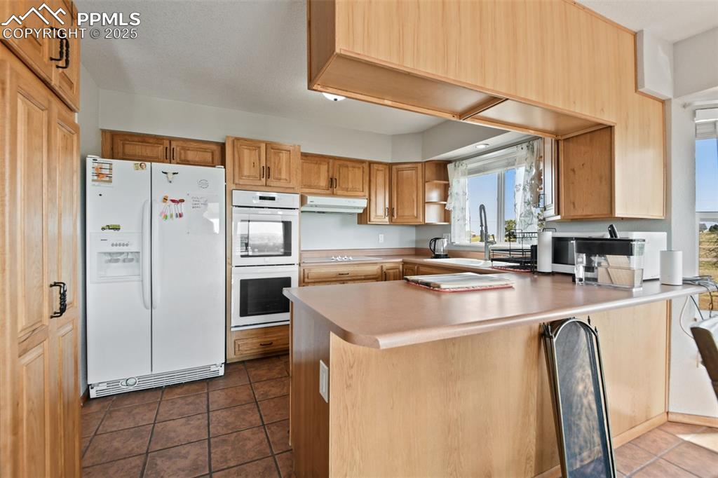 Image 15 of 40: Kitchen with white appliances, dark tile patterned floors, open shelves, a 