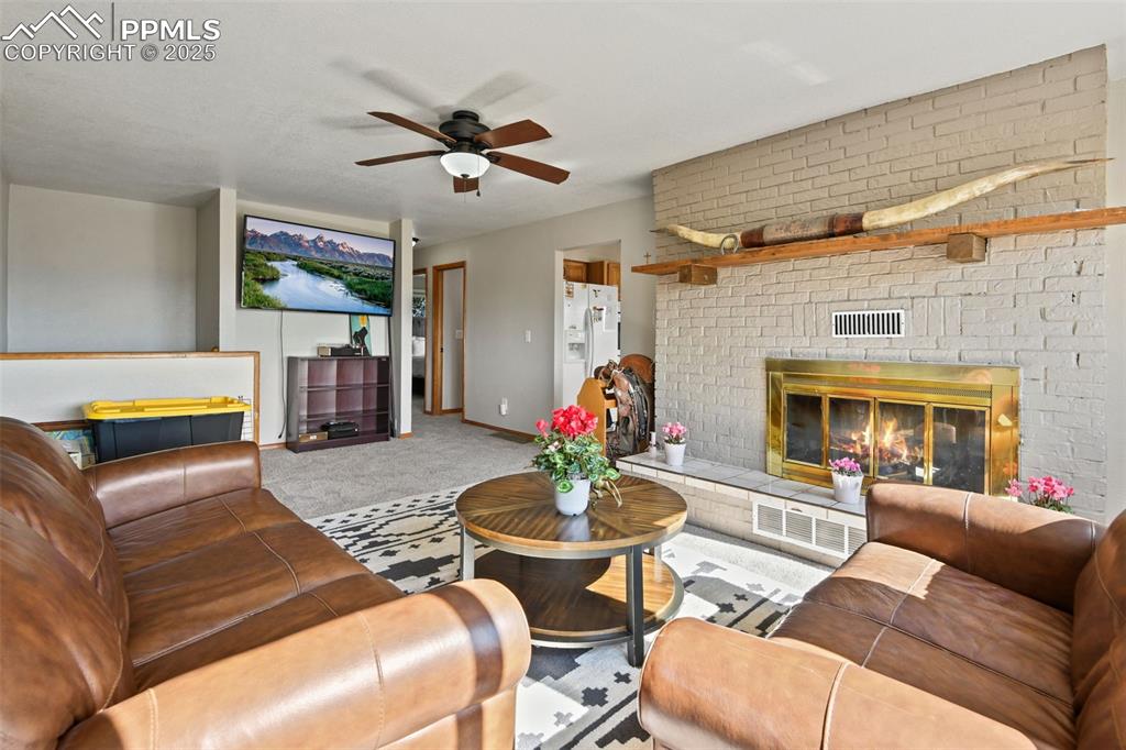 Image 7 of 40: Living area with a fireplace, carpet flooring, and a ceiling fan