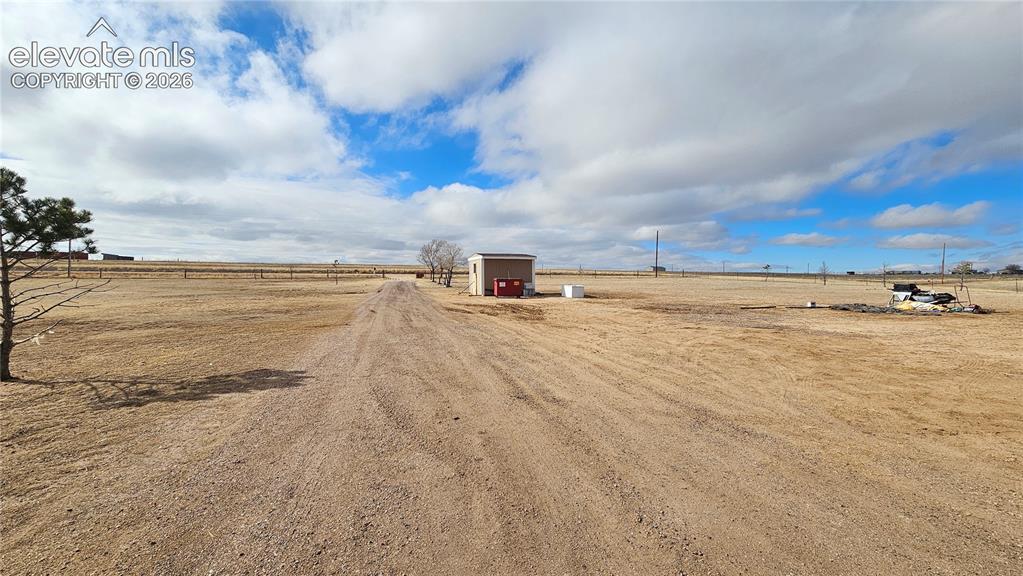 Image 12 of 48: Expansive unpaved lot with distant fencing, a small utility building, and s