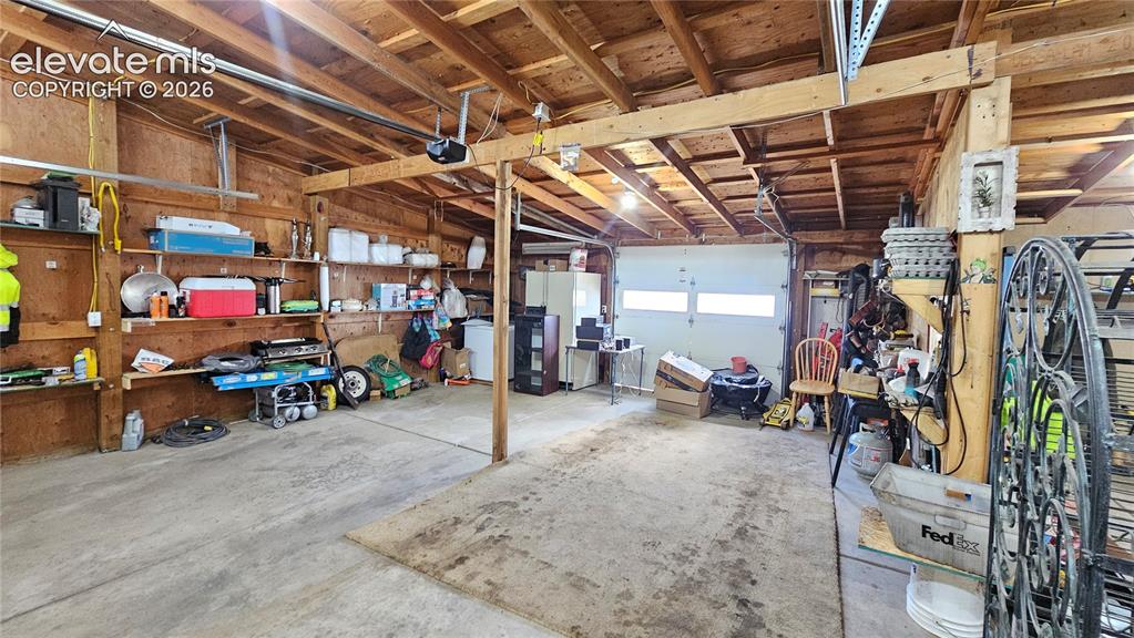 Image 38 of 48: Spacious garage with exposed wood beam ceiling, concrete flooring, built-in
