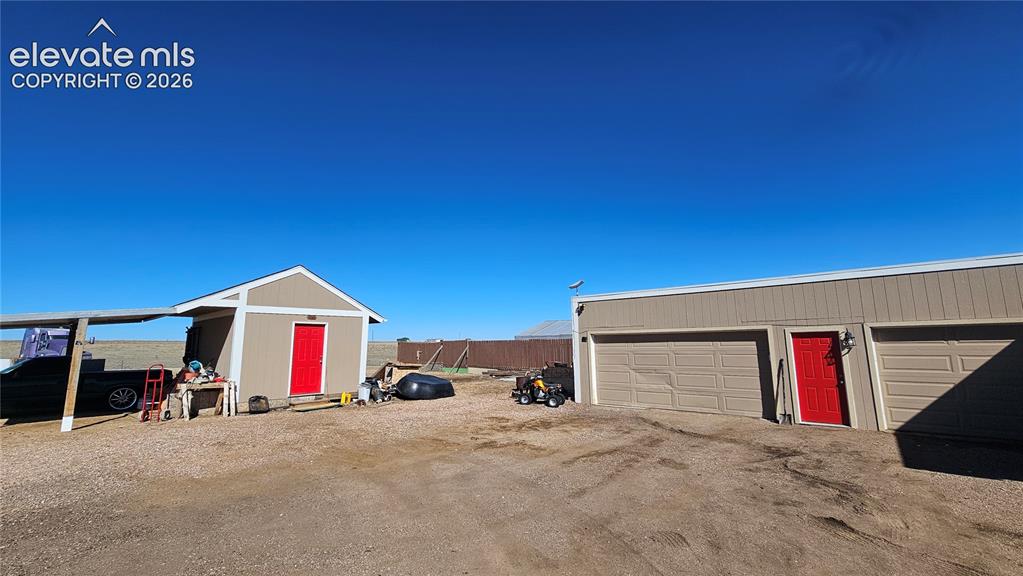 Image 44 of 48: Detached multi-car garage with overhead doors and a red entry door, complem