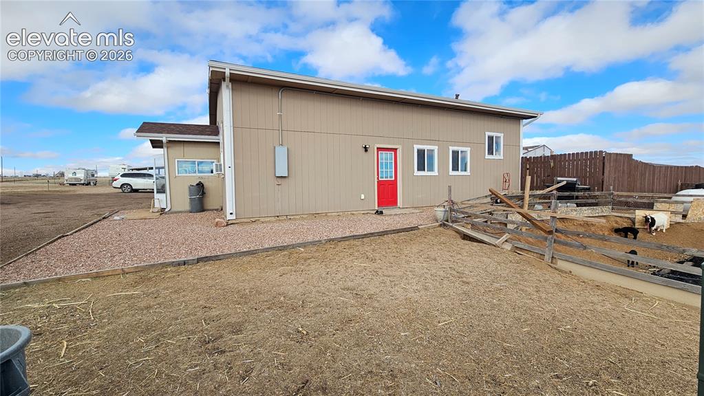 Image 9 of 48: Single-story structure with tan siding, a red entry door, white trim, and m