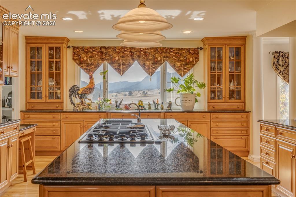 Image 18 of 32: Kitchen with glass insert cabinets, pendant lighting, dark stone countertop