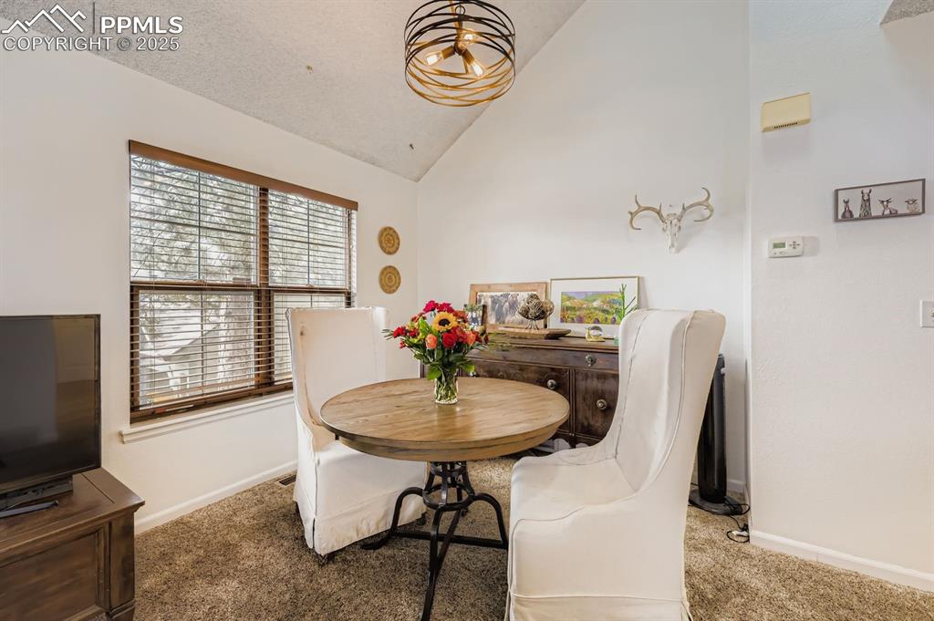 Image 11 of 25: Dining room with vaulted ceiling and carpet flooring