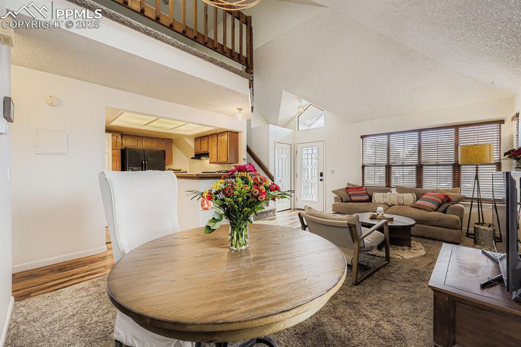 Image 12 of 25: Dining room with a textured ceiling, high vaulted ceiling, and light wood f