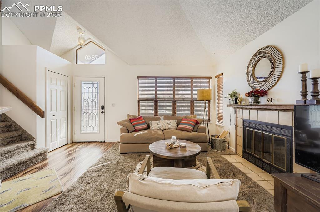 Image 5 of 25: Living room with a textured ceiling, lofted ceiling, stairway, a tile firep