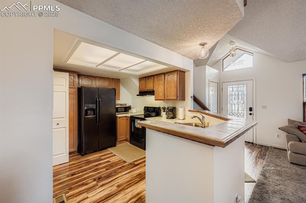 Image 6 of 25: Kitchen featuring black appliances, a peninsula, light wood finished floors