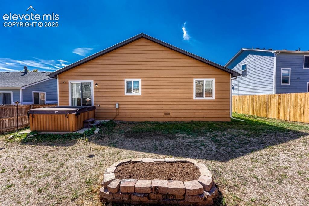 Image 28 of 35: Rear view of home and backyard with raised flower bed, concrete patio. Hot