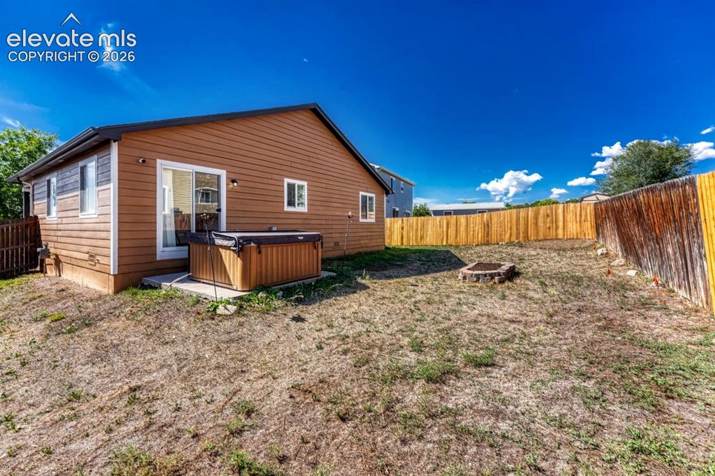 Image 29 of 35: Private backyard featuring a stone fire pit, wood fencing, and a concrete p