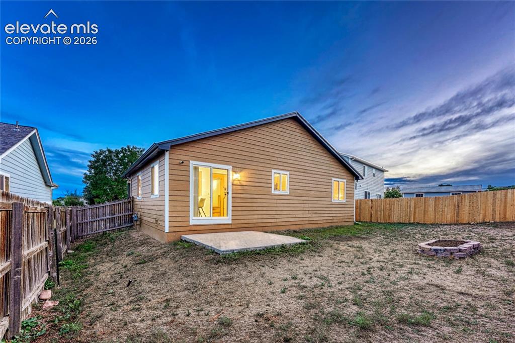Image 9 of 35: Large fenced backyard with sprinkler system, patio, and raised flower bed.