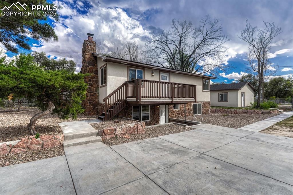 Image 2 of 50: View of front of house with stucco siding, stone siding, a deck, a chimney,
