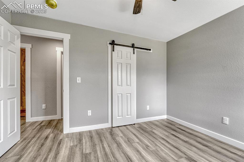 Image 23 of 50: Unfurnished bedroom with a barn door, a textured wall, light wood-style flo