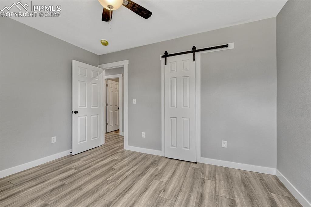 Image 24 of 50: Unfurnished bedroom featuring a barn door, light wood-type flooring, and a 