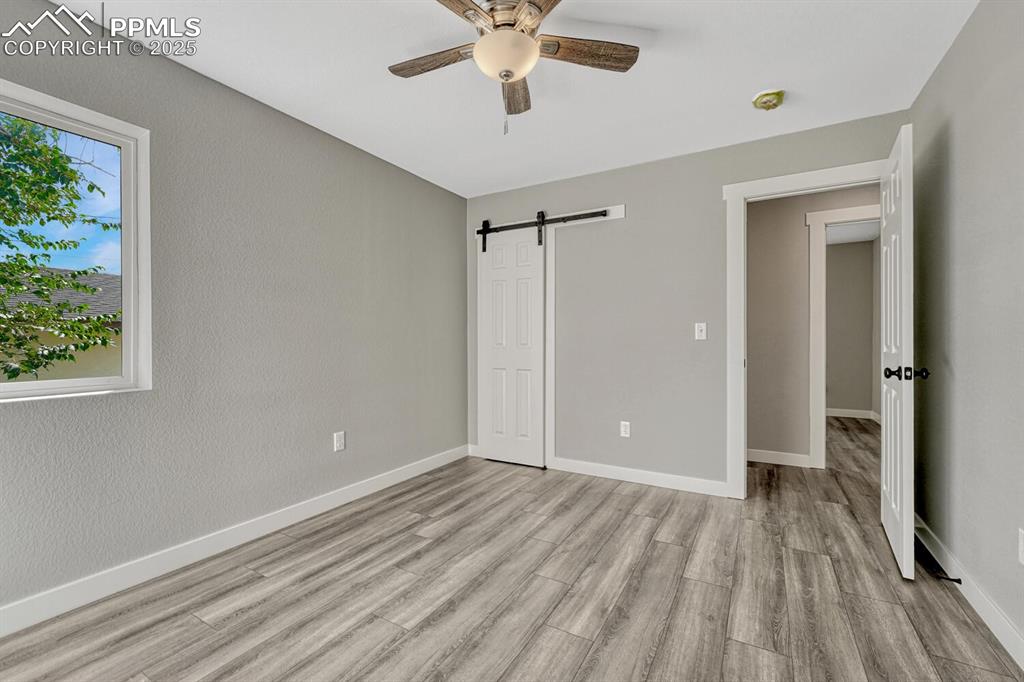 Image 28 of 50: Unfurnished bedroom with a barn door, light wood-style flooring, and a ceil