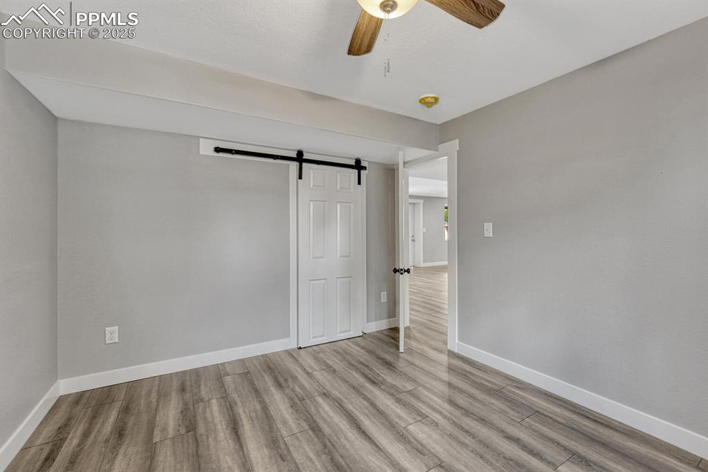 Image 42 of 50: Unfurnished bedroom featuring a barn door, wood finished floors, and ceilin