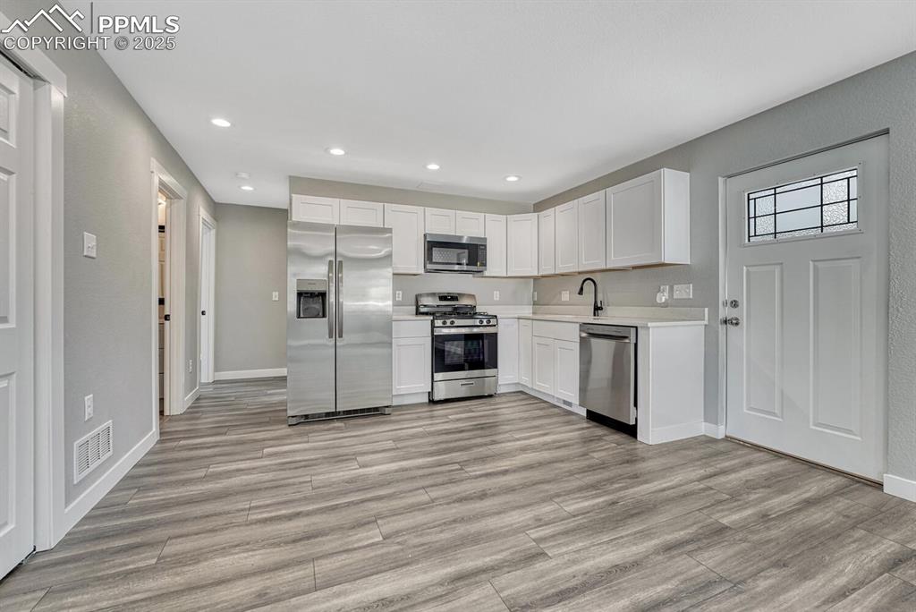 Image 7 of 50: Kitchen featuring white cabinetry, stainless steel appliances, light counte