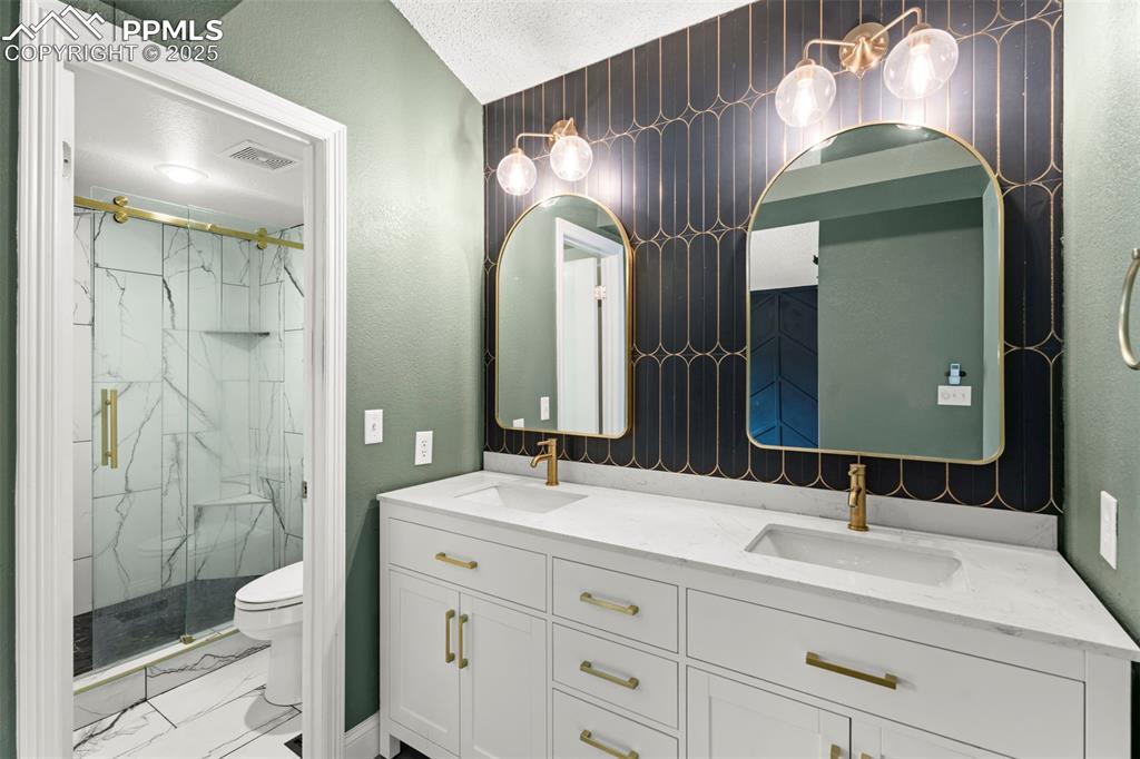Image 13 of 30: Bathroom with a marble finish shower, marble look tiles, double vanity, a t