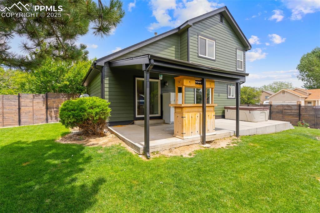 Image 24 of 30: Back of house featuring a fenced backyard, a hot tub, and a patio area