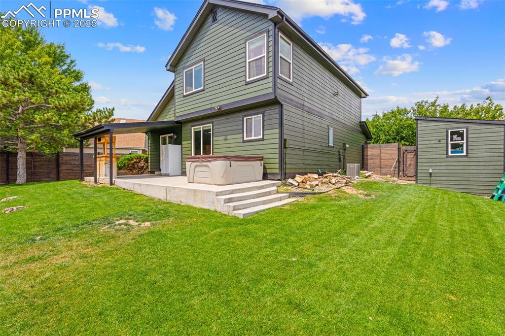 Image 25 of 30: Back of house featuring a fenced backyard, a hot tub, and a patio area