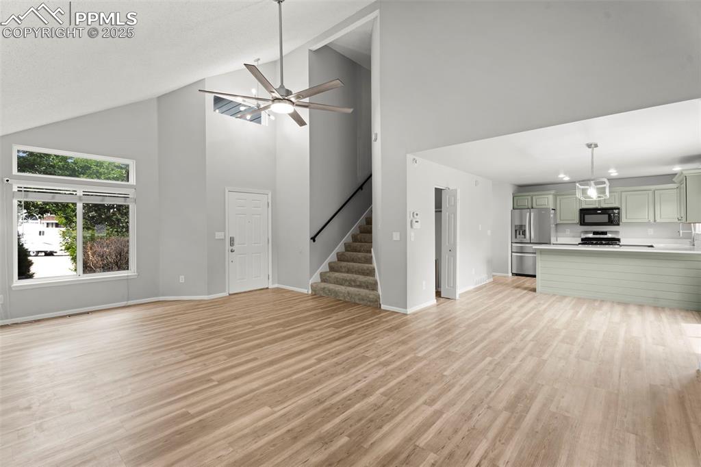 Image 7 of 30: Unfurnished living room with high vaulted ceiling, ceiling fan, light wood-