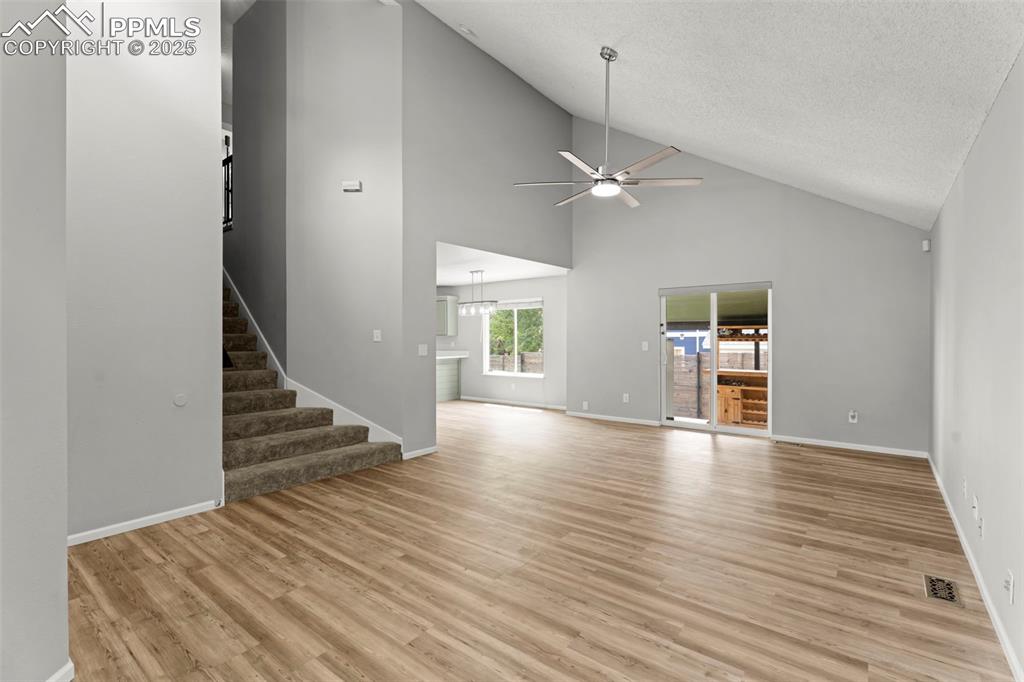 Image 8 of 30: Unfurnished living room with high vaulted ceiling, stairs, light wood-style