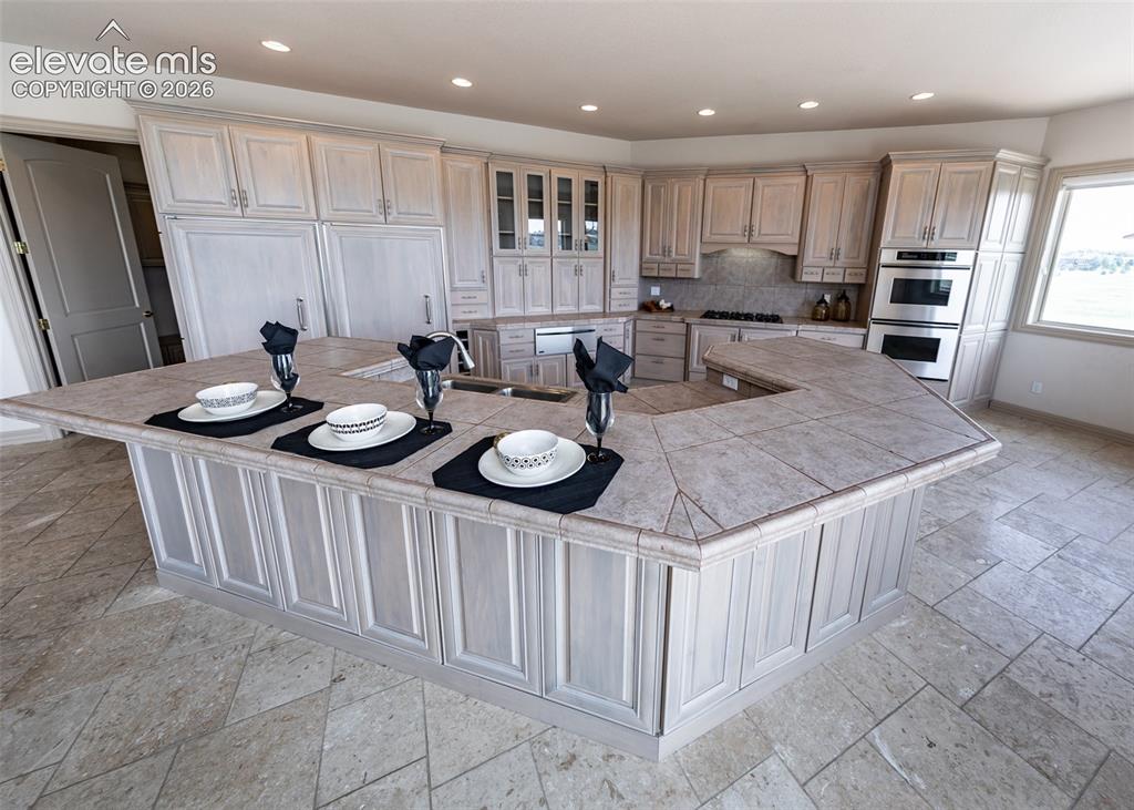 Image 12 of 50: Spacious kitchen featuring a large U-shaped island with a tiled countertop